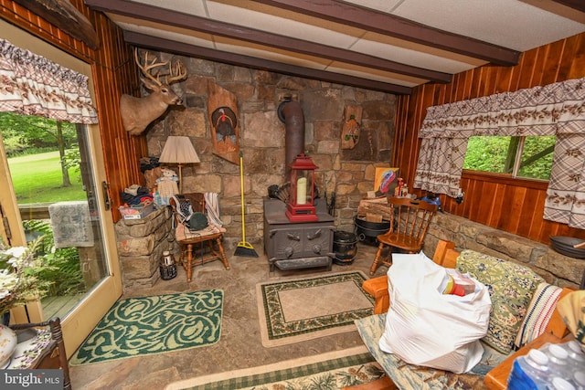 interior space with beam ceiling, wood walls, and a wood stove