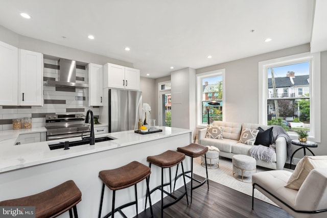 kitchen featuring light stone counters, dark hardwood / wood-style floors, sink, wall chimney exhaust hood, and appliances with stainless steel finishes