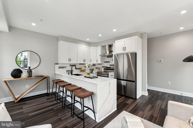 kitchen with white cabinets, backsplash, kitchen peninsula, stainless steel appliances, and wall chimney range hood