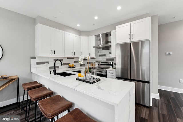 kitchen featuring appliances with stainless steel finishes, decorative backsplash, white cabinets, wall chimney exhaust hood, and sink