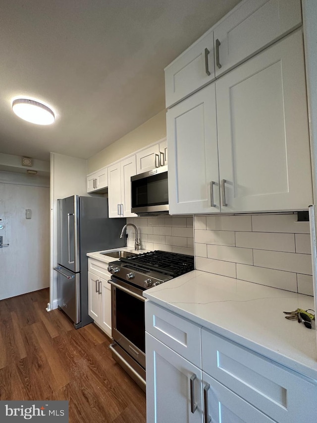 kitchen with white cabinetry, dark wood-style flooring, backsplash, a sink, and appliances with stainless steel finishes