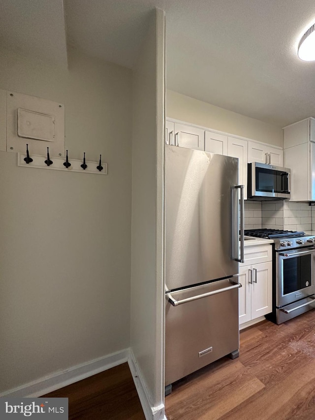 kitchen featuring white cabinets, baseboards, wood finished floors, tasteful backsplash, and appliances with stainless steel finishes