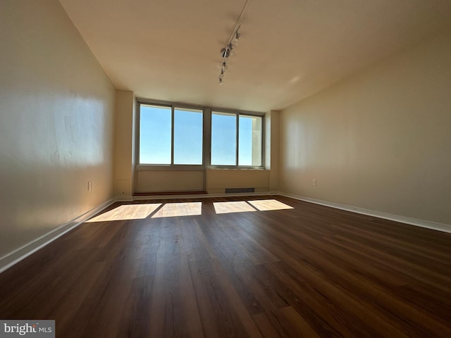 spare room with baseboards, dark wood-style flooring, rail lighting, and visible vents
