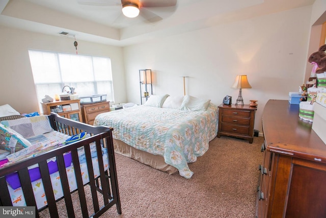 carpeted bedroom featuring ceiling fan and a tray ceiling