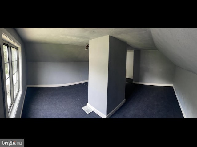 bonus room with lofted ceiling, dark colored carpet, and a textured ceiling