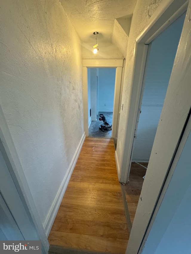 hall with wood-type flooring and vaulted ceiling