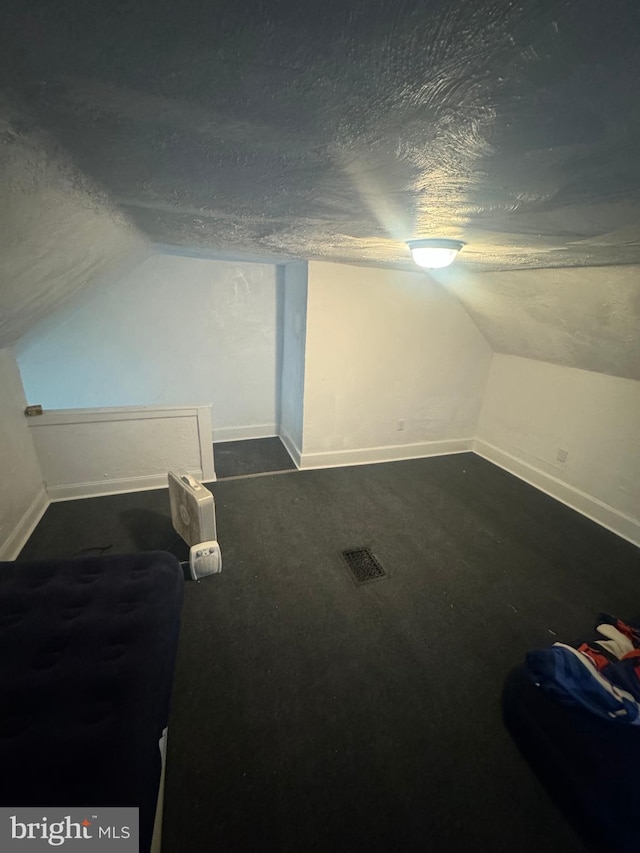 bonus room featuring dark carpet, lofted ceiling, and a textured ceiling