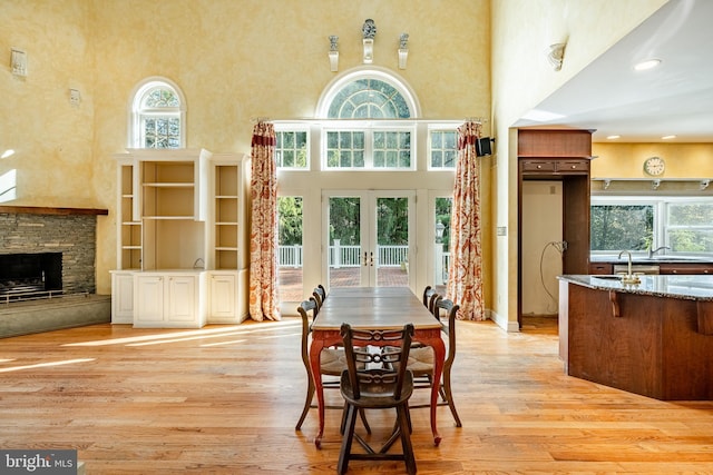 dining room featuring a fireplace, a high ceiling, light hardwood / wood-style floors, and french doors