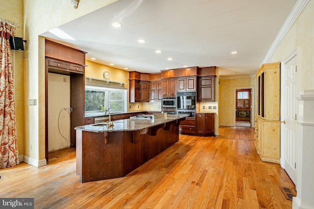 kitchen with stainless steel appliances, sink, light hardwood / wood-style flooring, stone counters, and a breakfast bar area