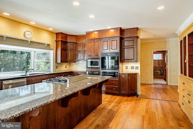 kitchen featuring sink, stainless steel appliances, light hardwood / wood-style flooring, stone countertops, and a breakfast bar area