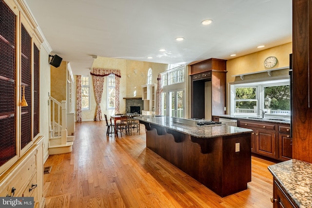 kitchen featuring a breakfast bar, sink, light hardwood / wood-style flooring, dark stone countertops, and a center island