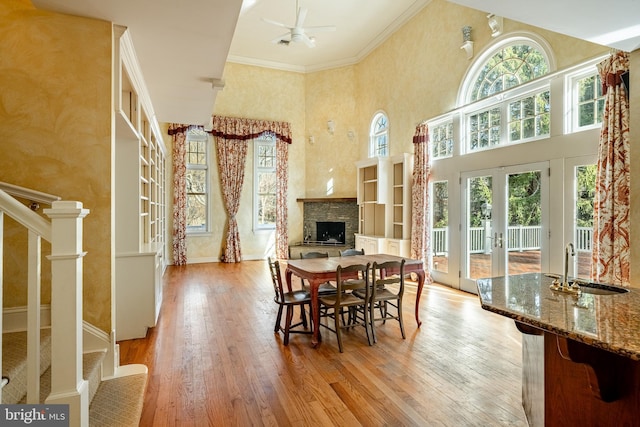 dining room with french doors, ceiling fan, ornamental molding, a fireplace, and light hardwood / wood-style floors