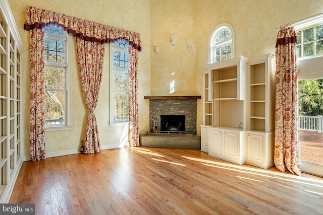 unfurnished living room with a fireplace, a high ceiling, light hardwood / wood-style flooring, and plenty of natural light