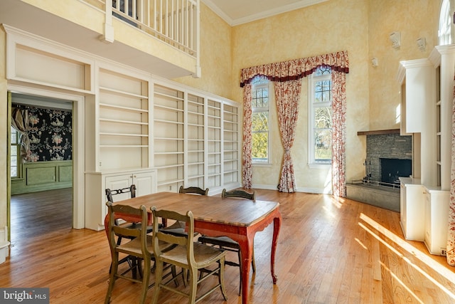 dining room with hardwood / wood-style floors, built in shelves, a towering ceiling, a fireplace, and ornamental molding