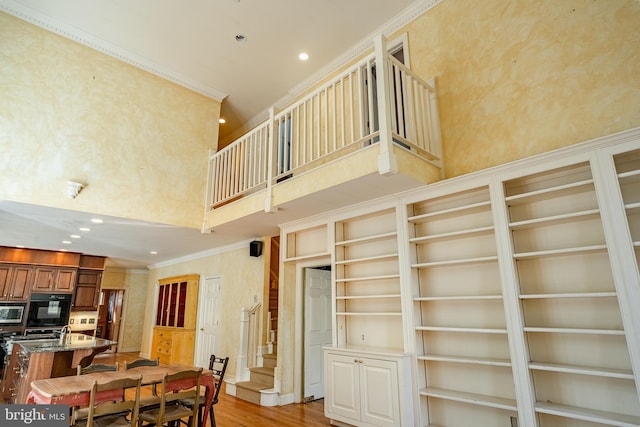 dining space with a towering ceiling, light wood-type flooring, built in features, and crown molding