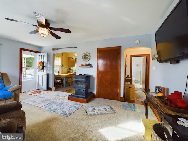 carpeted living room featuring a wood stove and ceiling fan