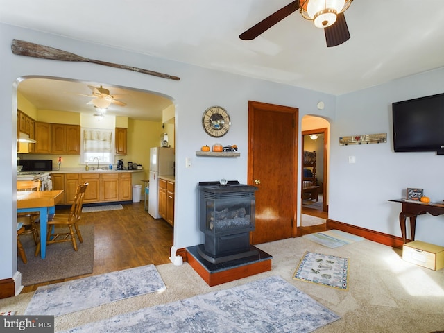 living room featuring ceiling fan, sink, dark hardwood / wood-style flooring, and a wood stove