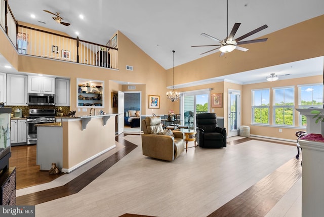 living room with light hardwood / wood-style floors, sink, ceiling fan with notable chandelier, high vaulted ceiling, and crown molding