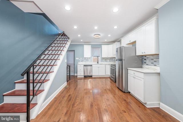 kitchen featuring ornamental molding, sink, white cabinetry, appliances with stainless steel finishes, and light hardwood / wood-style floors