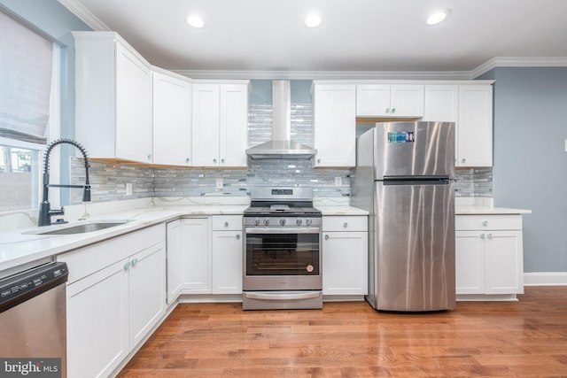 kitchen featuring white cabinets, appliances with stainless steel finishes, light wood-type flooring, wall chimney exhaust hood, and sink