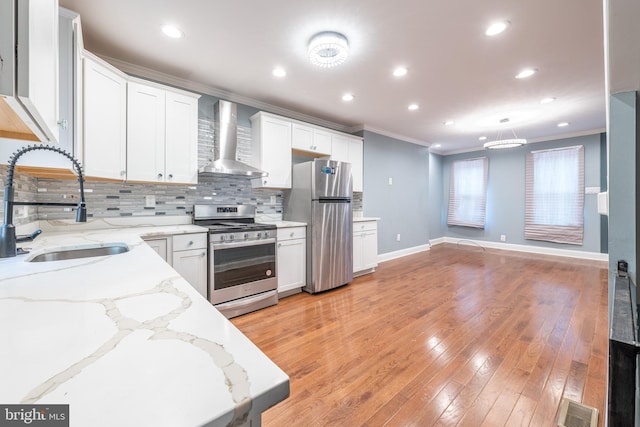 kitchen featuring wall chimney range hood, sink, stainless steel appliances, white cabinets, and light hardwood / wood-style flooring