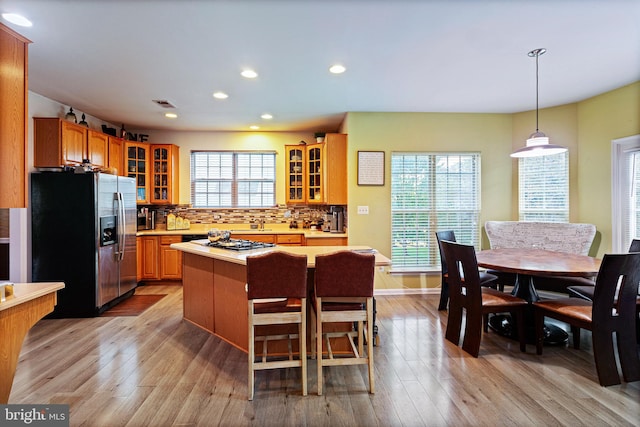 kitchen with stainless steel refrigerator with ice dispenser, a wealth of natural light, light hardwood / wood-style floors, and a center island