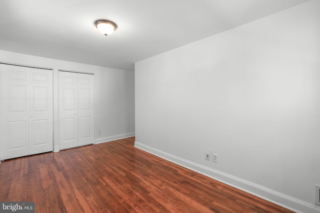 unfurnished bedroom featuring dark wood-type flooring and multiple closets