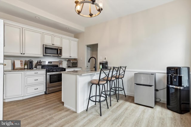 kitchen featuring a chandelier, white cabinetry, stainless steel appliances, light stone countertops, and light hardwood / wood-style floors