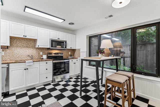 kitchen featuring decorative backsplash, white cabinets, and appliances with stainless steel finishes