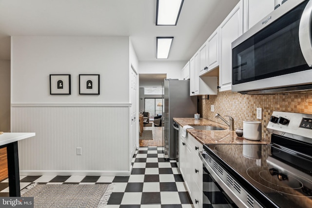 kitchen with appliances with stainless steel finishes, white cabinetry, backsplash, wooden walls, and sink