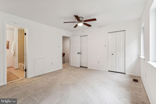 unfurnished bedroom featuring ceiling fan, light colored carpet, two closets, and ensuite bath