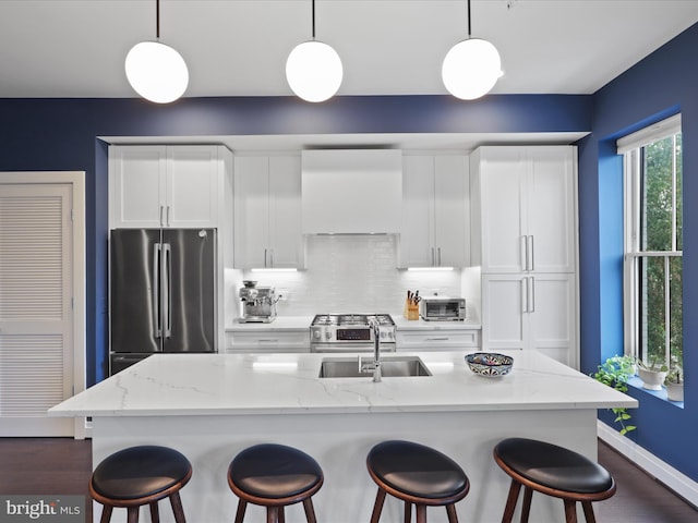 kitchen featuring pendant lighting, stainless steel appliances, an island with sink, and white cabinets