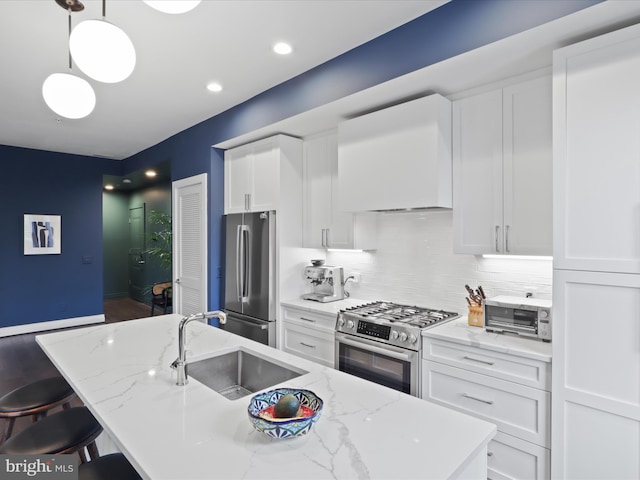 kitchen featuring a kitchen island with sink, white cabinets, hanging light fixtures, appliances with stainless steel finishes, and light stone countertops