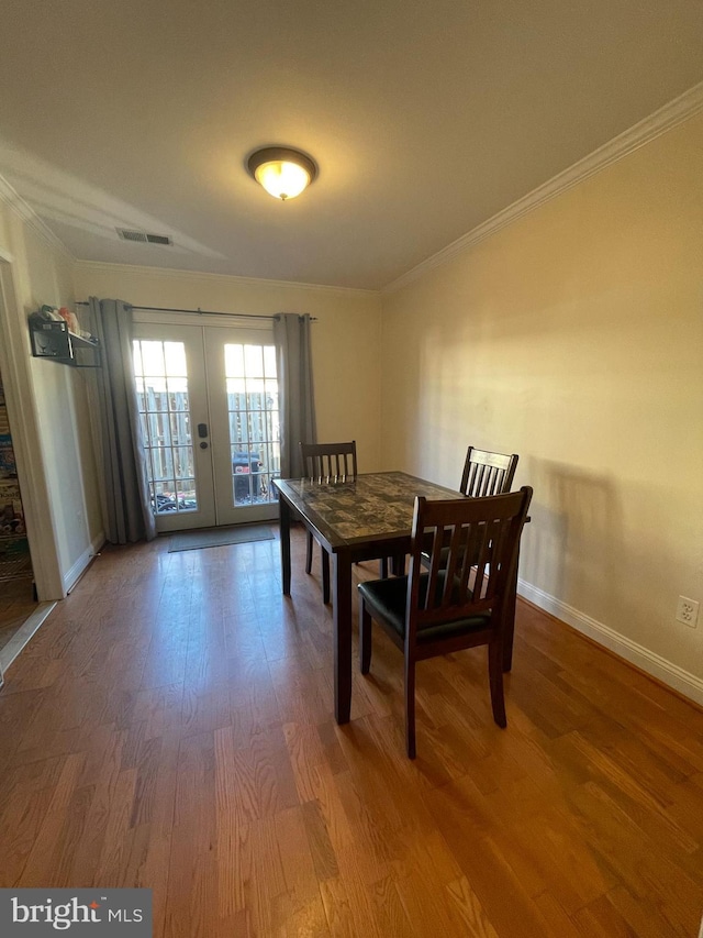 dining space with french doors, crown molding, visible vents, wood finished floors, and baseboards