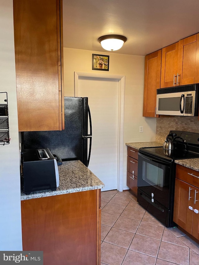 kitchen featuring light tile patterned floors, decorative backsplash, stainless steel microwave, brown cabinets, and black / electric stove