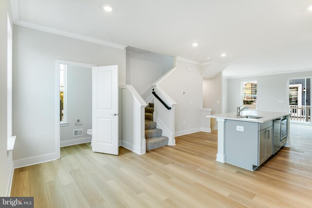 kitchen featuring gray cabinetry, light hardwood / wood-style floors, crown molding, a kitchen island with sink, and sink