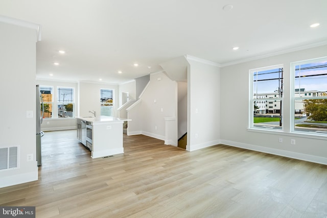 interior space featuring sink, an island with sink, light hardwood / wood-style flooring, crown molding, and stainless steel fridge