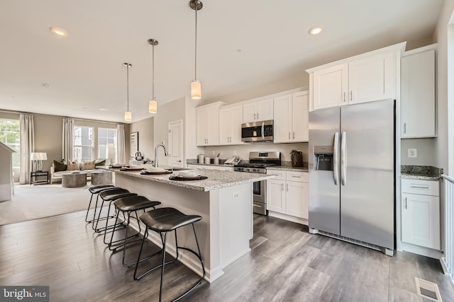 kitchen featuring decorative light fixtures, an island with sink, appliances with stainless steel finishes, and white cabinetry