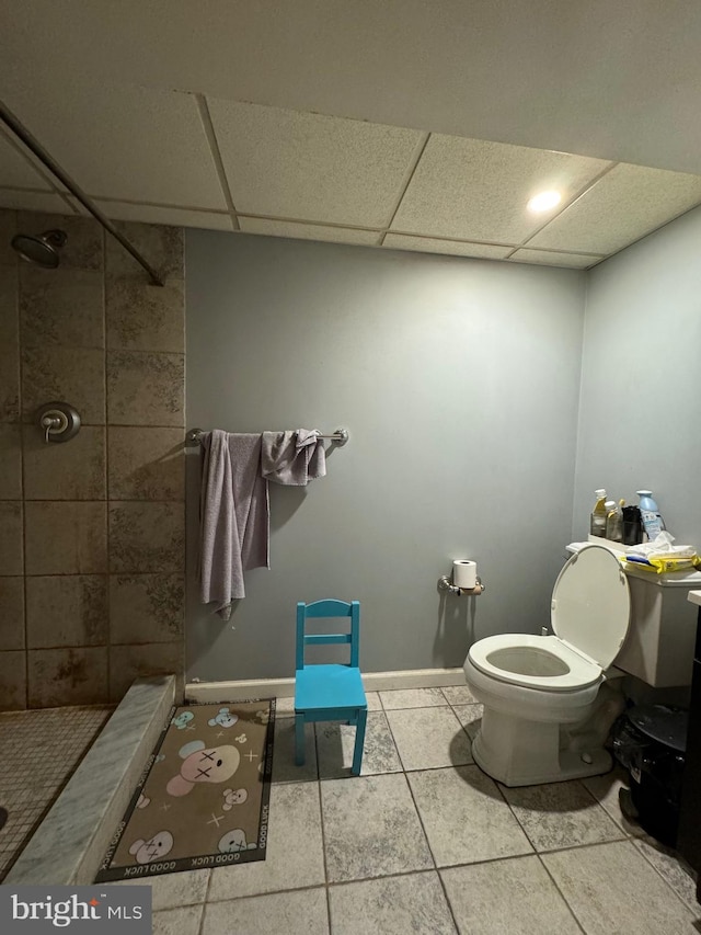 bathroom featuring toilet, a drop ceiling, tile patterned flooring, and a tile shower