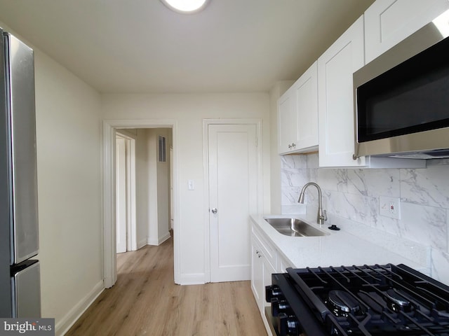 kitchen featuring white cabinetry, tasteful backsplash, stainless steel appliances, light wood-type flooring, and sink