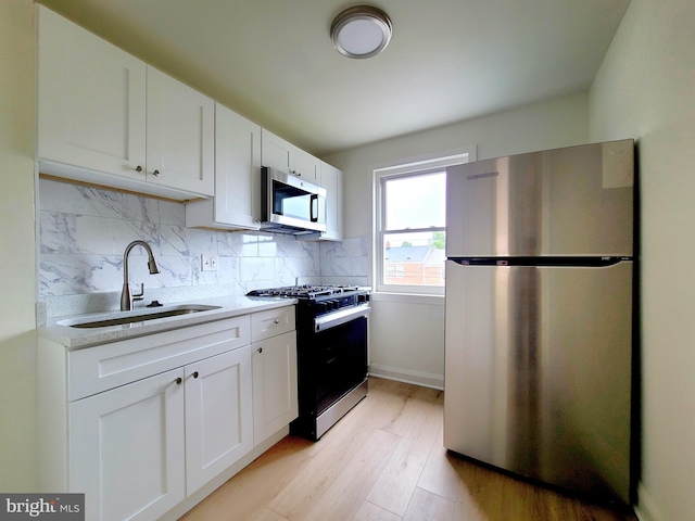 kitchen featuring a sink, tasteful backsplash, stainless steel appliances, white cabinets, and light wood-style floors
