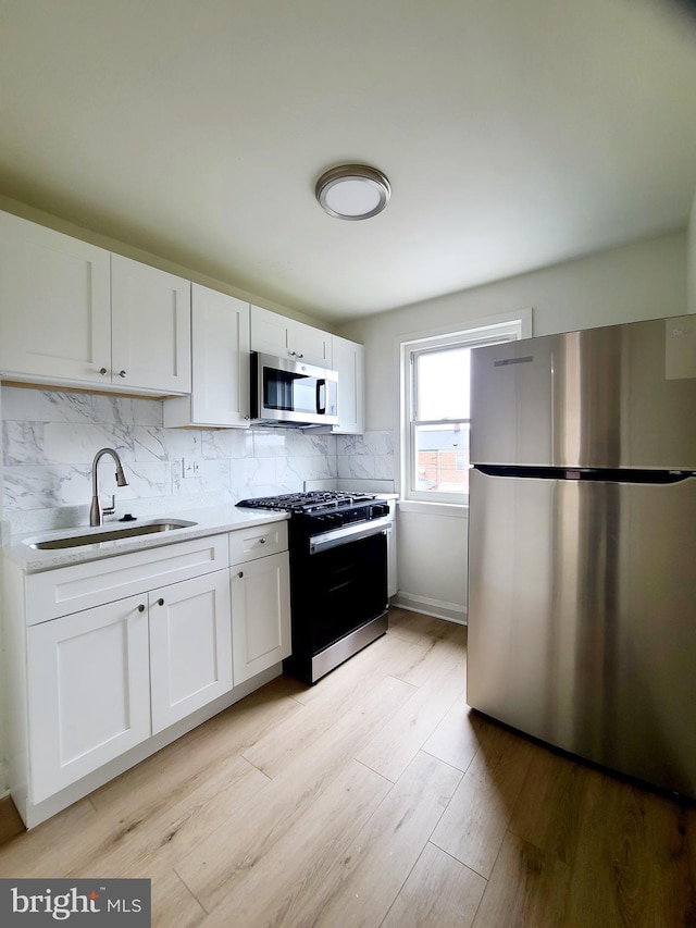 kitchen with sink, light hardwood / wood-style flooring, white cabinetry, appliances with stainless steel finishes, and decorative backsplash