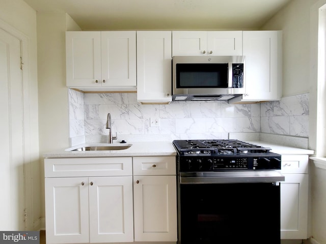 kitchen featuring white cabinets, range with gas stovetop, stainless steel microwave, tasteful backsplash, and a sink