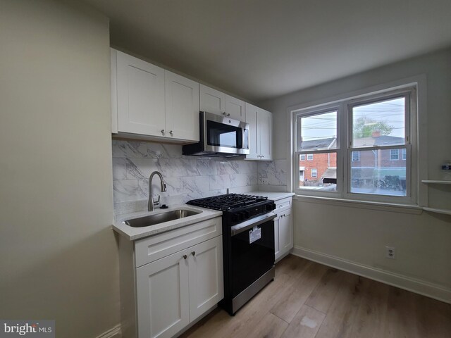 kitchen with sink, white cabinets, light hardwood / wood-style flooring, stainless steel appliances, and decorative backsplash