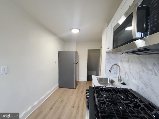 kitchen with decorative backsplash, white cabinets, baseboards, stainless steel appliances, and light wood-type flooring