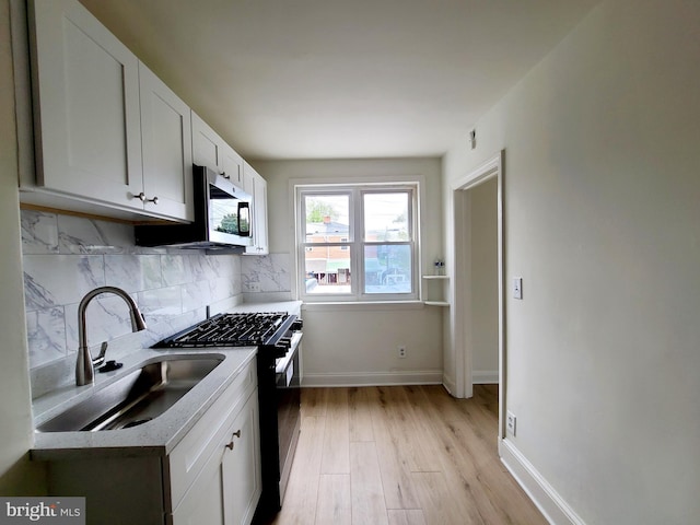 kitchen featuring decorative backsplash, range with gas stovetop, stainless steel microwave, white cabinetry, and a sink