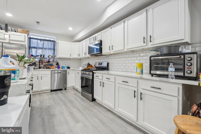 kitchen with light stone countertops, stainless steel appliances, tasteful backsplash, white cabinetry, and light hardwood / wood-style flooring