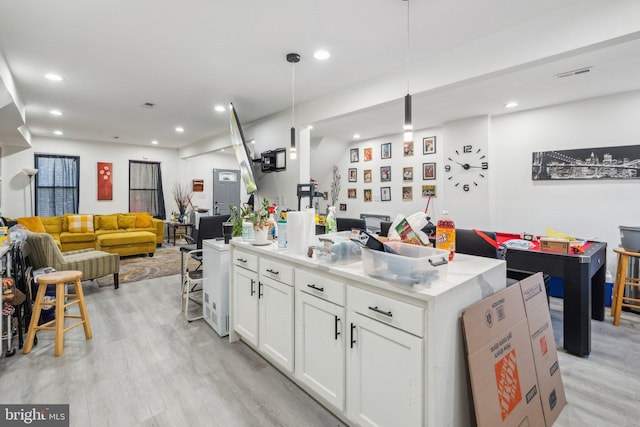 kitchen featuring pendant lighting, an island with sink, light wood-type flooring, and white cabinetry