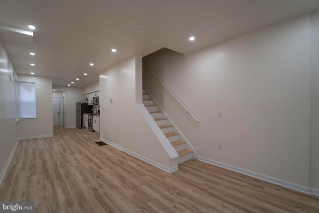 basement featuring light hardwood / wood-style flooring and stainless steel fridge