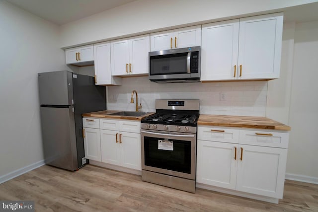 kitchen featuring appliances with stainless steel finishes, white cabinetry, wooden counters, light wood-type flooring, and sink